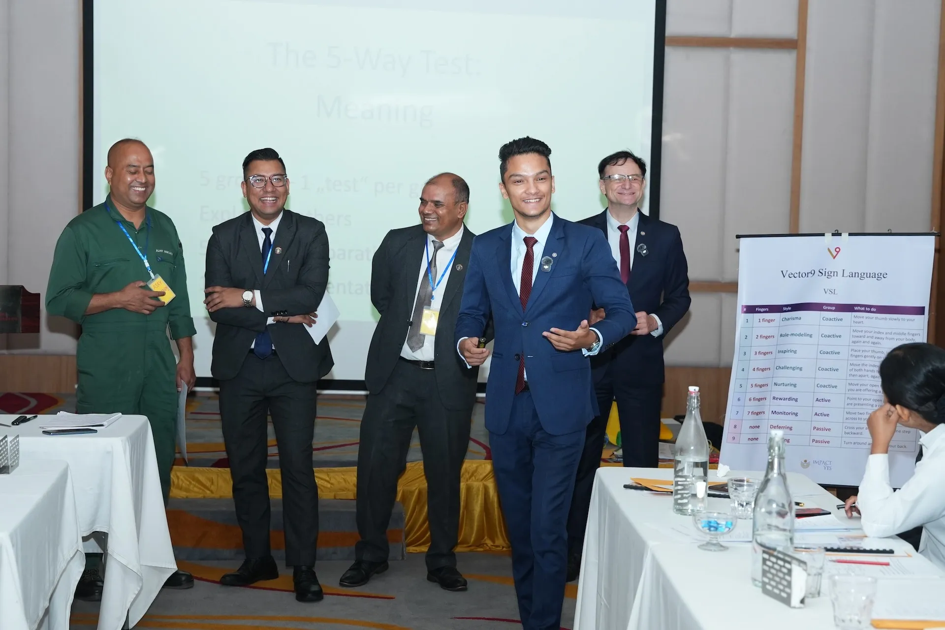 Kovid Panthy laughing with participants at the front of the room, a Vector9 Sign Language chart on the easel beside him.