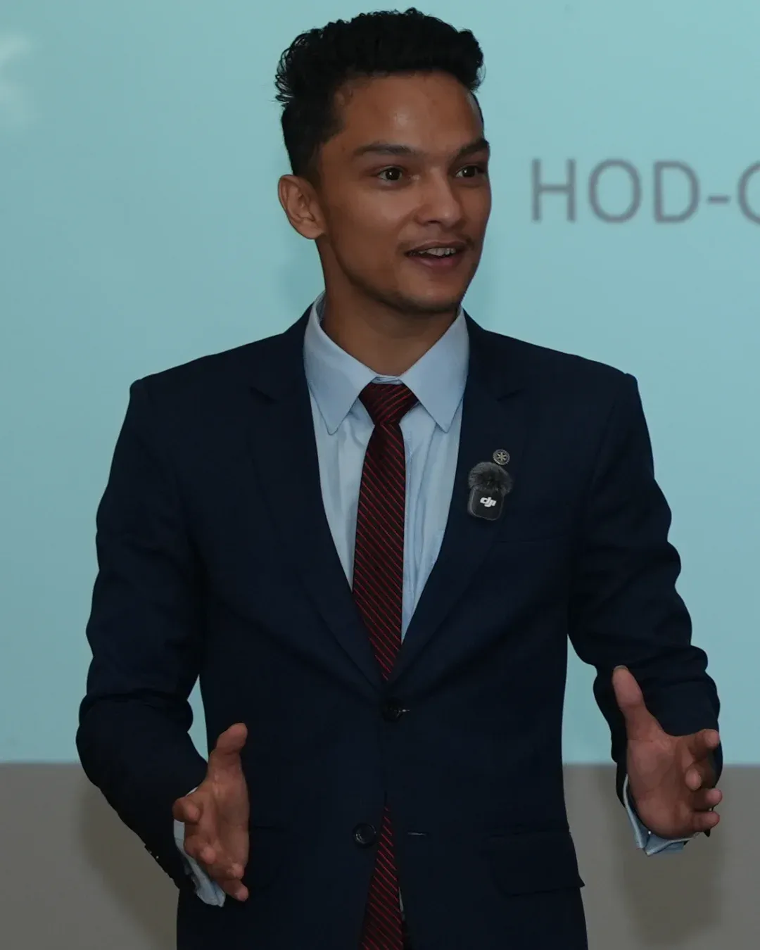 Kovid Panthy speaking with both hands open, a presentation screen behind him.