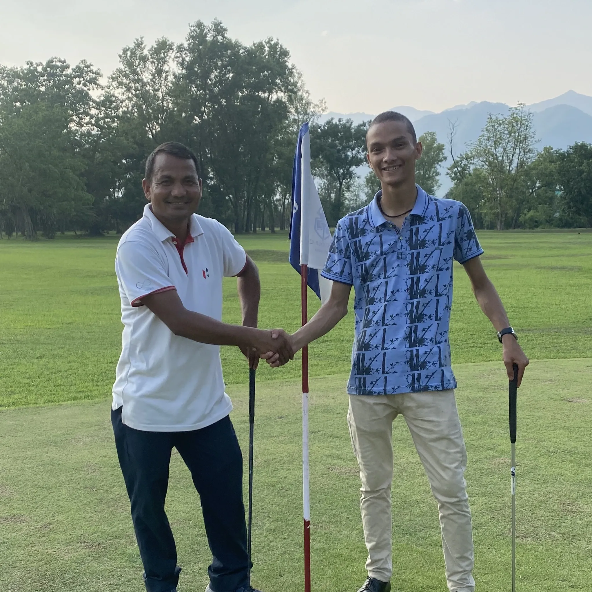 Kovid Panthy shaking hands with another golfer on the green, clubs and pin flag in hand.