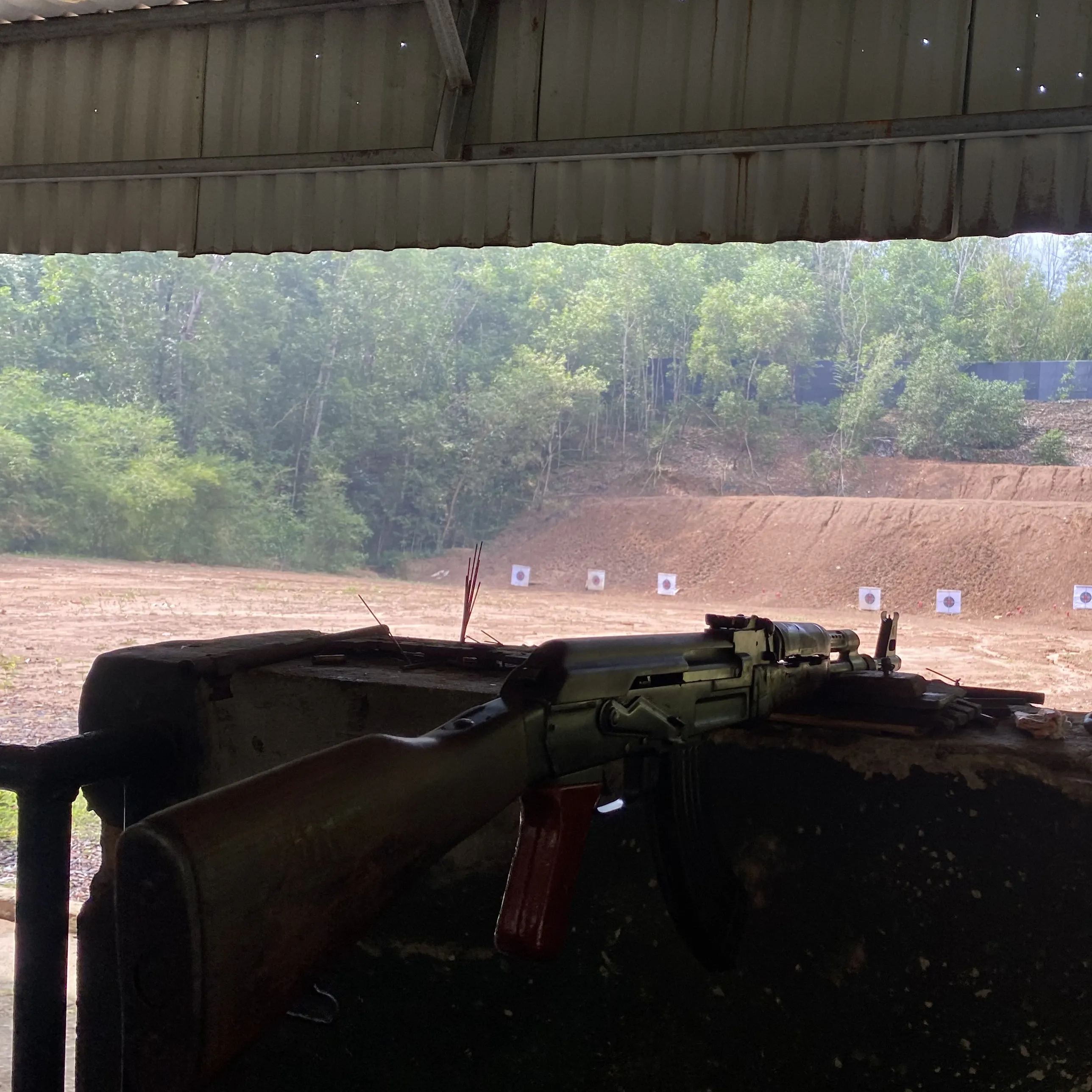 A rifle resting on the bench of an outdoor range, paper targets set out downrange.