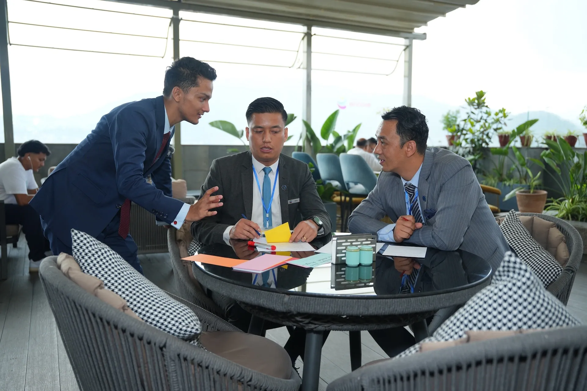 Kovid Panthy leaning over a rooftop table mid-discussion with two seated men, papers and notes between them.