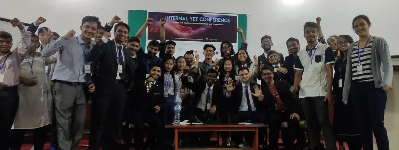 Attendees of the Internal YET Conference gathered under the event banner, arms raised.